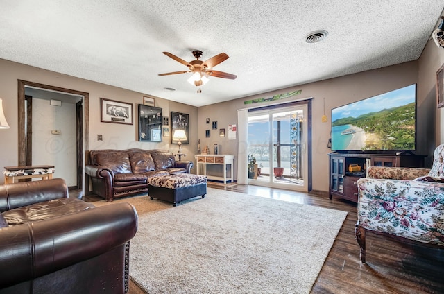 living area featuring dark wood-type flooring, visible vents, ceiling fan, and a textured ceiling