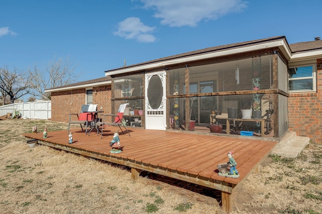 rear view of house with a sunroom, a wooden deck, fence, and brick siding