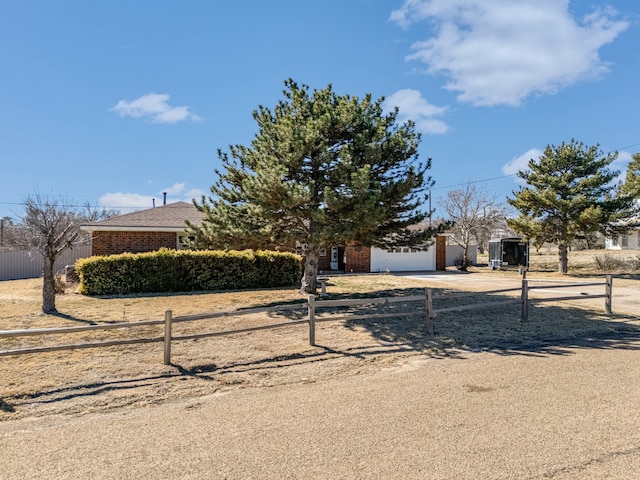 view of property hidden behind natural elements with driveway, an attached garage, fence, and brick siding