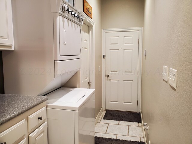 laundry area featuring stacked washer and clothes dryer, cabinets, and light tile patterned flooring