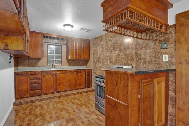 kitchen featuring a textured ceiling, a sink, baseboards, brown cabinets, and gas stove