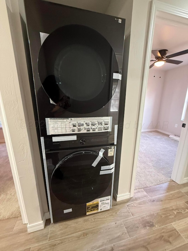 clothes washing area featuring ceiling fan, laundry area, carpet floors, wood finished floors, and stacked washer / drying machine