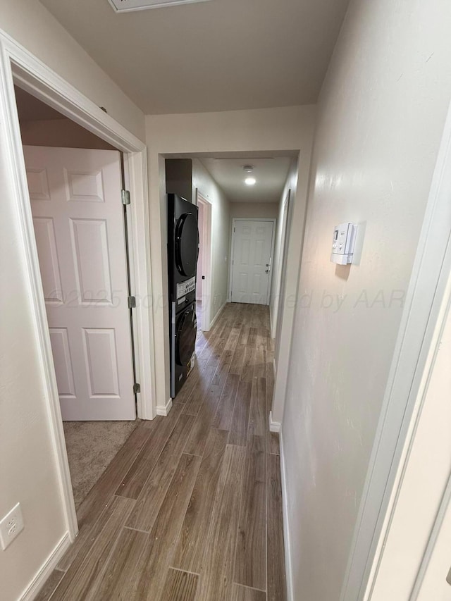 hallway with dark wood-style floors, stacked washer and clothes dryer, and baseboards