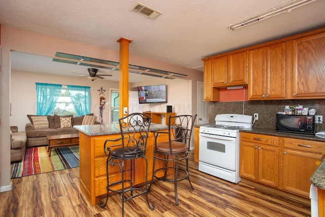 kitchen featuring white gas range, ceiling fan, dark wood-style flooring, black microwave, and open floor plan