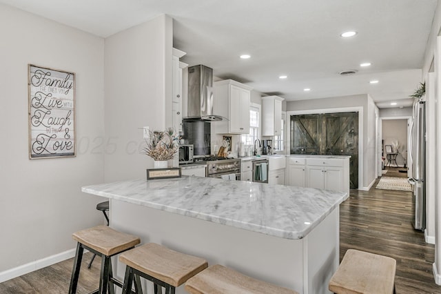 kitchen with wall chimney exhaust hood, white cabinets, appliances with stainless steel finishes, a breakfast bar area, and baseboards