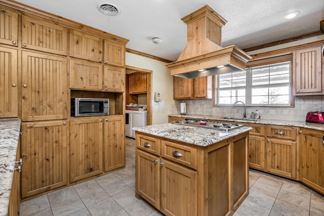 kitchen with washer and dryer, a kitchen island, sink, light stone countertops, and stainless steel appliances