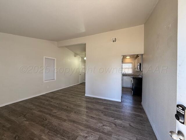 empty room with lofted ceiling, dark wood-type flooring, visible vents, and baseboards