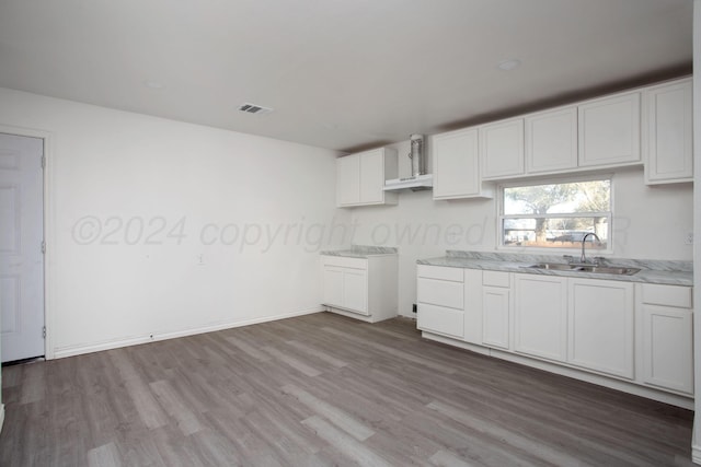 kitchen with a sink, wood finished floors, wall chimney range hood, white cabinetry, and baseboards