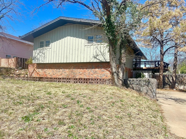 view of side of home featuring brick siding, a lawn, a deck, and fence