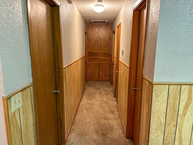 hallway with wooden walls, light carpet, and a textured ceiling