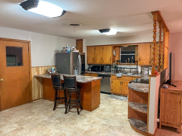 kitchen with stone counters, appliances with stainless steel finishes, a breakfast bar, kitchen peninsula, and a textured ceiling