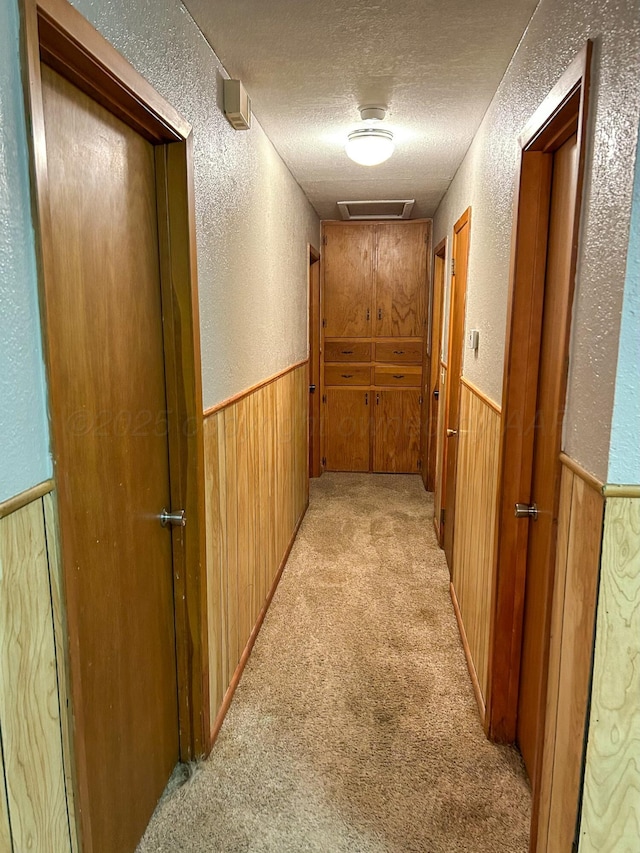 hallway featuring light carpet, wooden walls, and a textured ceiling