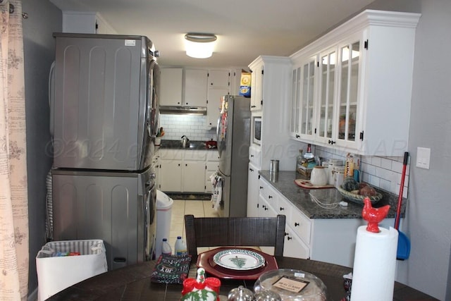 kitchen featuring decorative backsplash, stacked washer / drying machine, freestanding refrigerator, built in microwave, and white cabinetry