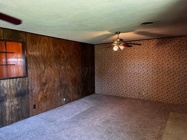 empty room with carpet, wood walls, a textured ceiling, and ceiling fan