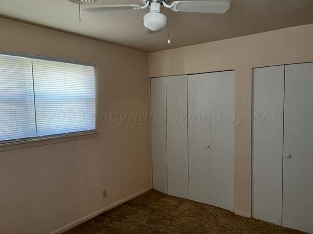 unfurnished bedroom featuring ceiling fan, two closets, and dark carpet