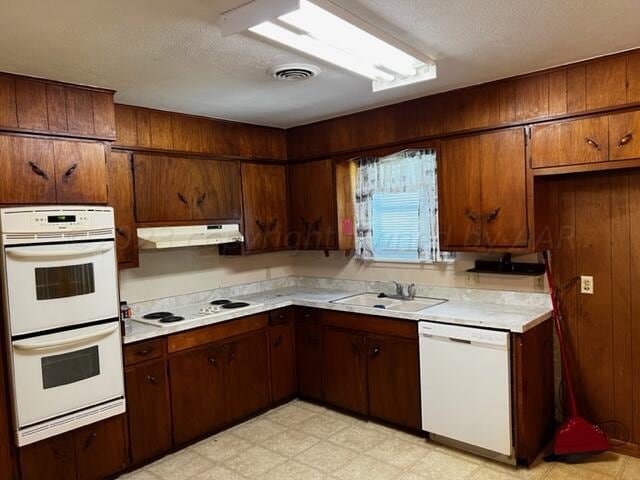 kitchen featuring a textured ceiling, wooden walls, sink, and white appliances