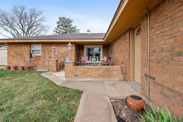 view of exterior entry with brick siding, a patio area, and a lawn