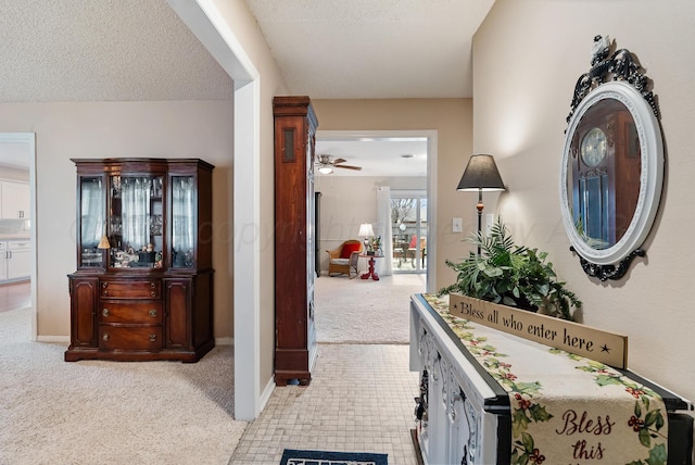hallway featuring a textured ceiling, baseboards, and light colored carpet
