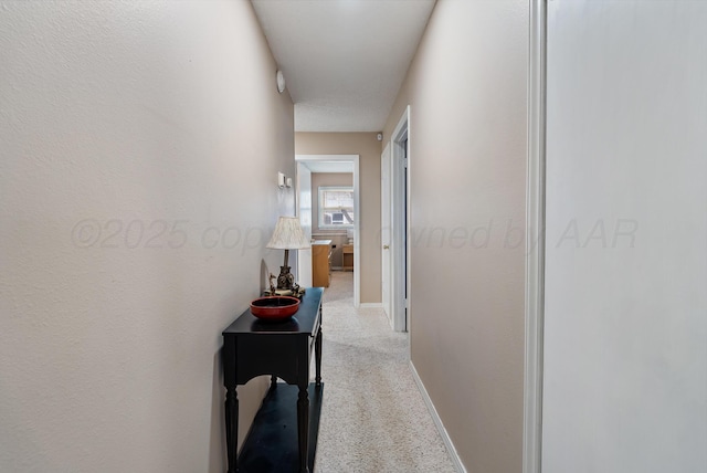 hallway with baseboards and light colored carpet