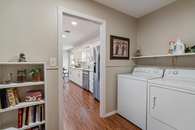 laundry room featuring laundry area, wood finished floors, a sink, separate washer and dryer, and recessed lighting