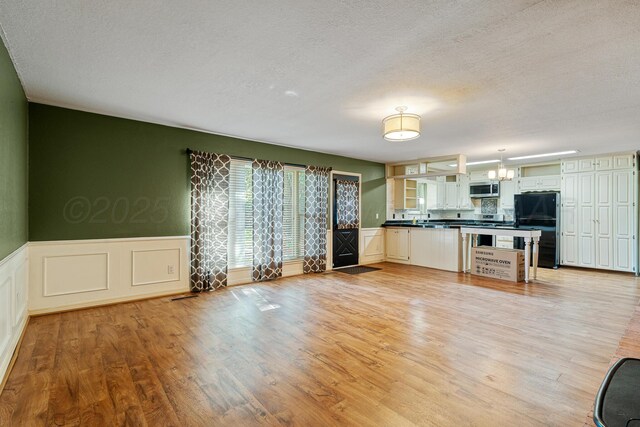 1604 Country Ln, Panhandle, TX 79068 - kitchen featuring stainless steel microwave, freestanding refrigerator, dark countertops, light wood finished floors, and a textured ceiling