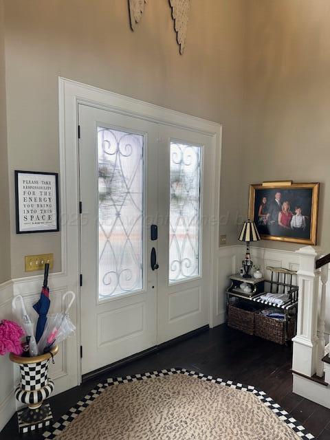 entrance foyer featuring wood finished floors, a decorative wall, french doors, and a wainscoted wall