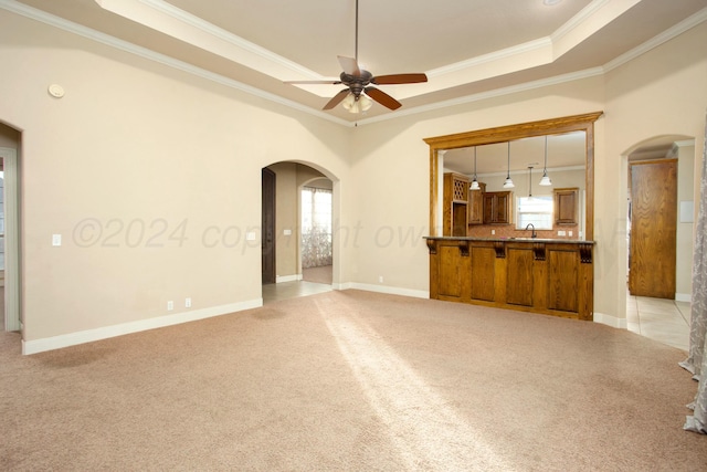 unfurnished living room with light carpet, sink, crown molding, ceiling fan, and a tray ceiling