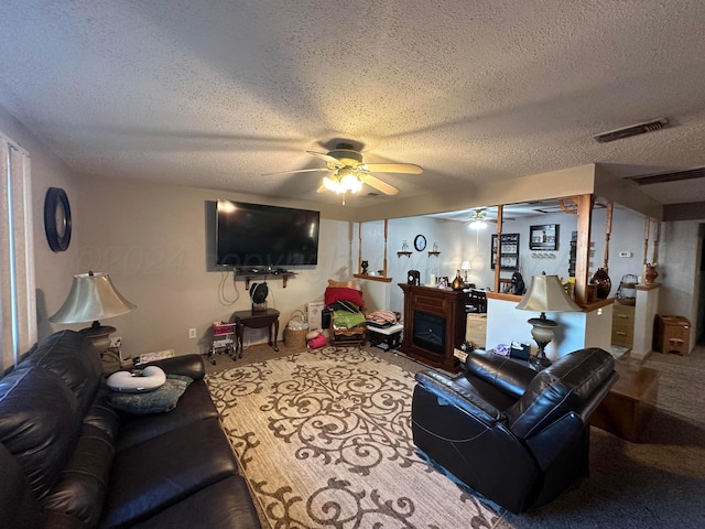 living room with a fireplace, ceiling fan, a textured ceiling, and carpet flooring