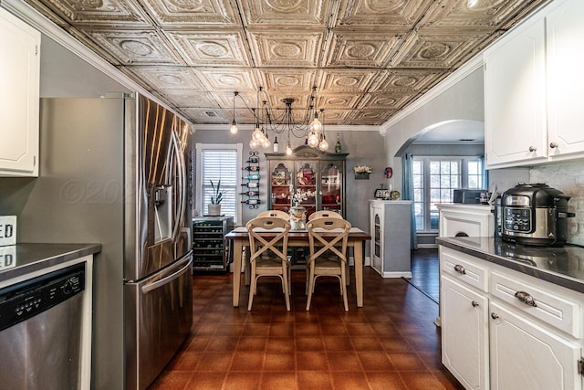 kitchen with an ornate ceiling, white cabinetry, stainless steel dishwasher, dark countertops, and decorative light fixtures