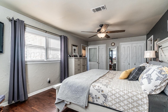 bedroom featuring baseboards, visible vents, a textured wall, dark wood-style floors, and two closets