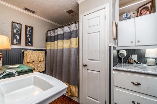 bathroom with a textured ceiling, ornamental molding, a sink, and visible vents