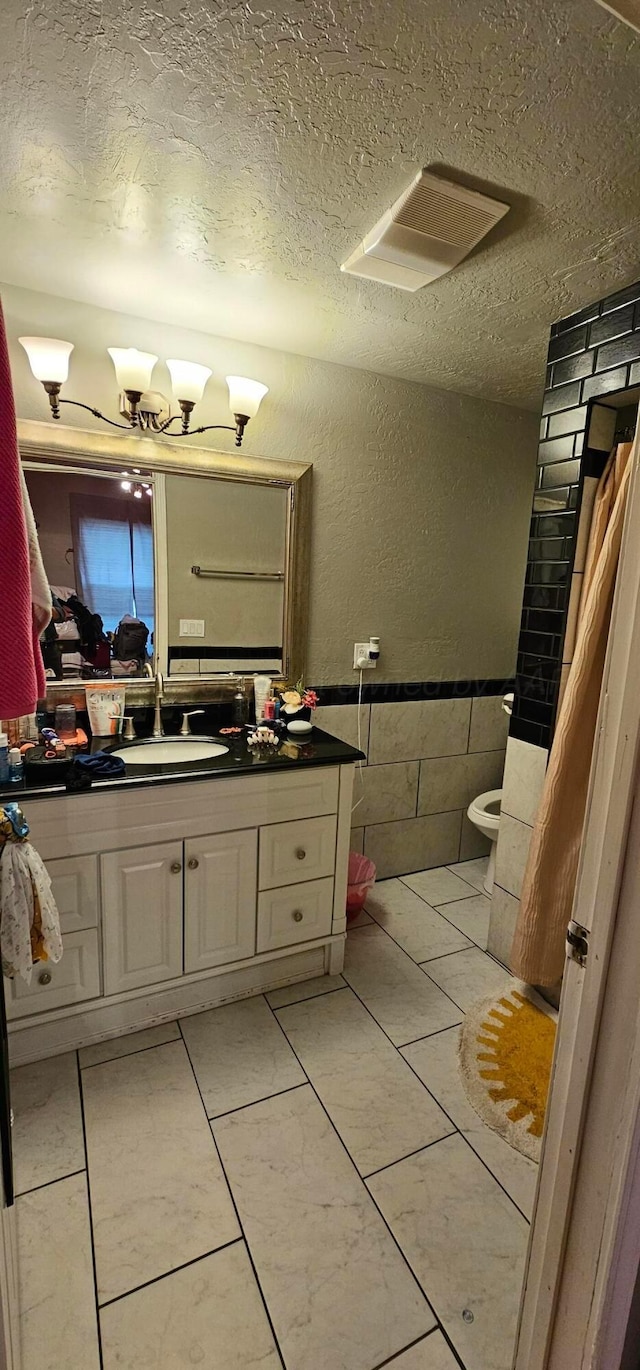 bathroom featuring tile walls, an inviting chandelier, vanity, a textured ceiling, and toilet