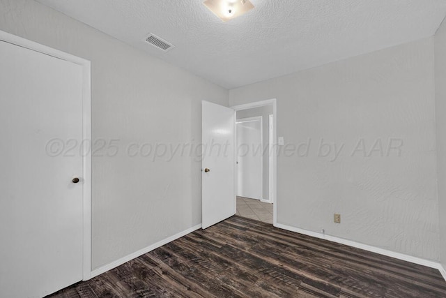 unfurnished bedroom featuring a textured ceiling, wood finished floors, visible vents, and baseboards