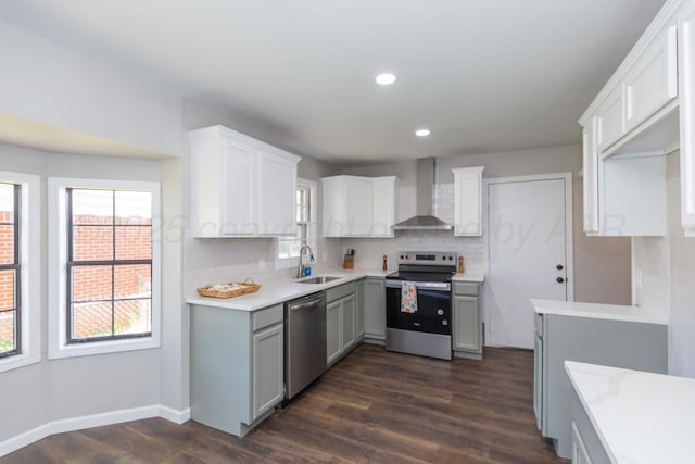 kitchen featuring wall chimney range hood, appliances with stainless steel finishes, a sink, dark wood finished floors, and backsplash