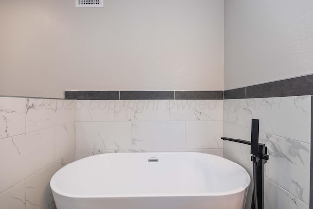 bathroom with a freestanding bath, tile walls, and visible vents