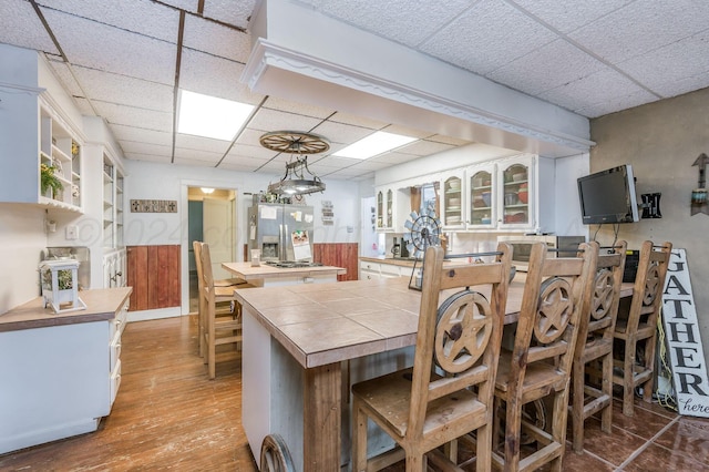 kitchen featuring light wood-type flooring, kitchen peninsula, decorative light fixtures, and a paneled ceiling