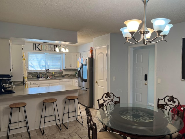 kitchen featuring white cabinets, stainless steel refrigerator with ice dispenser, a textured ceiling, sink, and tasteful backsplash