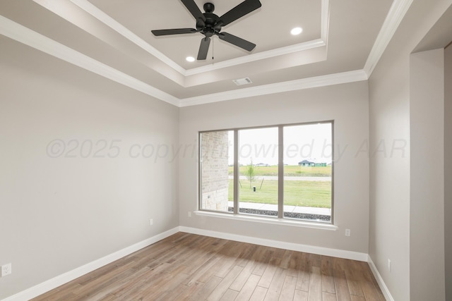 empty room featuring a ceiling fan, visible vents, wood finished floors, baseboards, and a tray ceiling