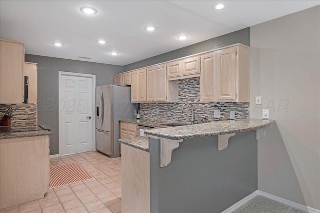 3507 Brennan Gdns, Amarillo, TX 79121 - kitchen with stainless steel appliances, a breakfast bar area, light brown cabinetry, a peninsula, and backsplash