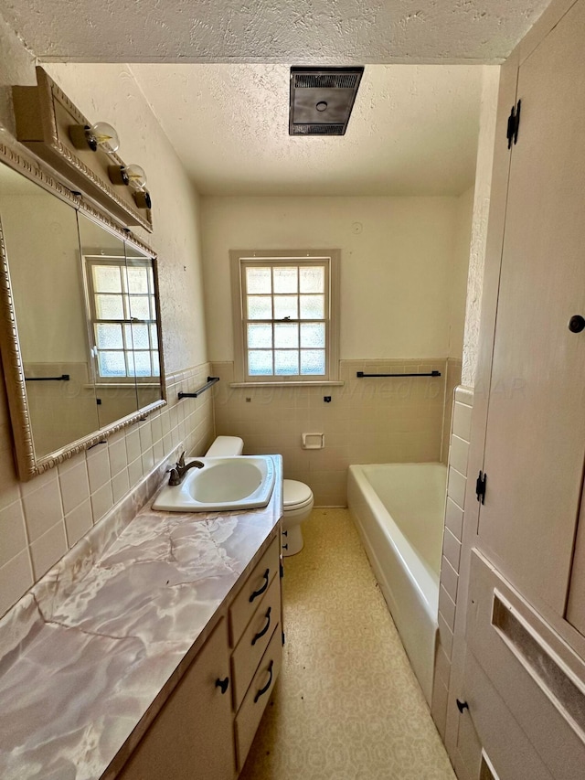 bathroom featuring tile walls, a bath, vanity, a textured ceiling, and toilet