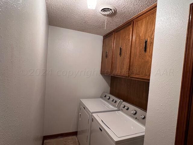 clothes washing area with a textured ceiling, cabinets, and washer and dryer