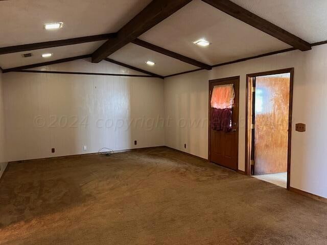 carpeted spare room with wooden walls and vaulted ceiling with beams