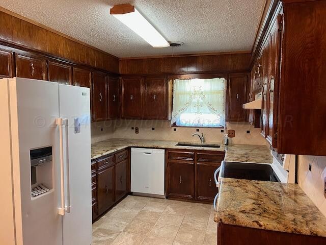 kitchen with sink, light stone counters, custom range hood, white appliances, and decorative backsplash