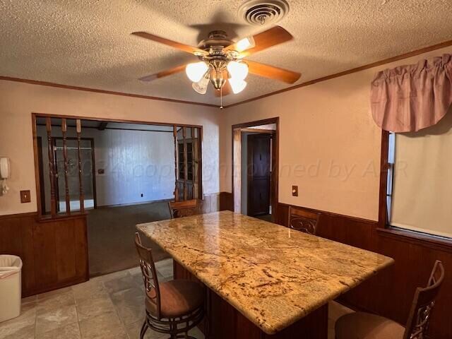 interior space with crown molding, a textured ceiling, wooden walls, a breakfast bar, and ceiling fan