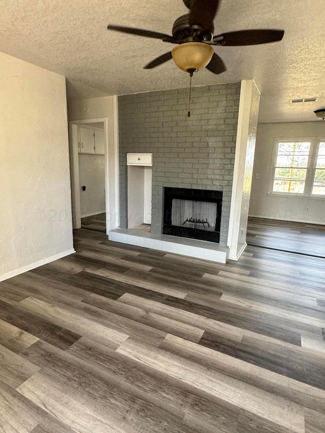 unfurnished living room featuring a fireplace, dark wood-type flooring, a textured ceiling, and ceiling fan