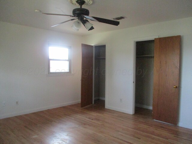 unfurnished bedroom with light wood-style floors, multiple closets, baseboards, and ceiling fan
