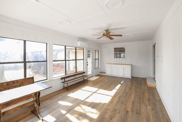 interior space with ceiling fan, a wall unit AC, and light hardwood / wood-style flooring