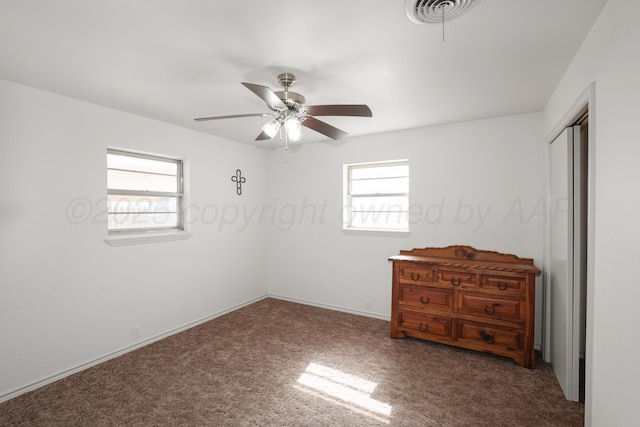 interior space with multiple windows, dark carpet, a closet, and ceiling fan