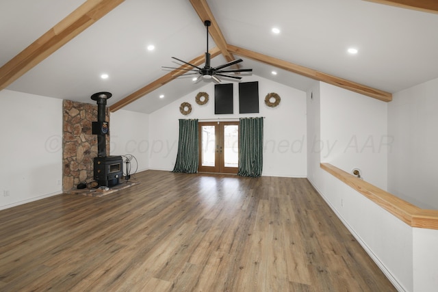 unfurnished living room with hardwood / wood-style floors, a wood stove, ceiling fan, beam ceiling, and french doors