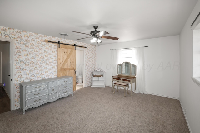 unfurnished bedroom with ensuite bathroom, a barn door, ceiling fan, and carpet flooring